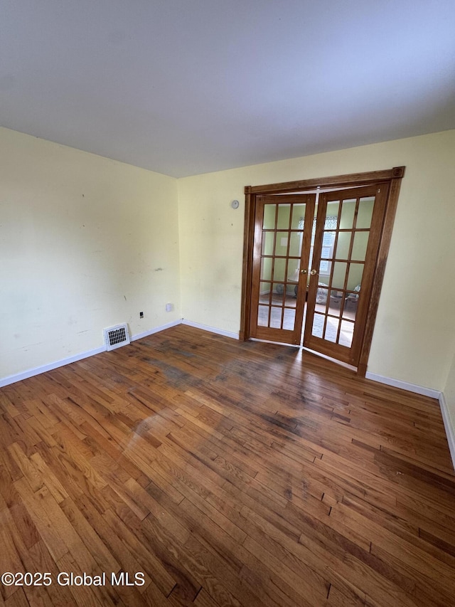 empty room featuring wood finished floors, french doors, visible vents, and baseboards