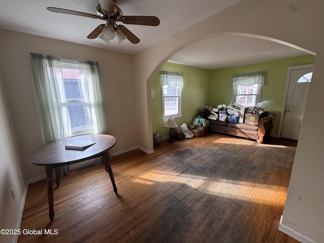 interior space with ceiling fan, baseboards, arched walkways, and wood finished floors