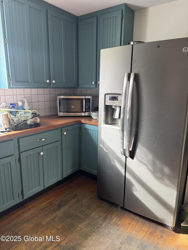 kitchen featuring blue cabinetry, dark wood-type flooring, butcher block countertops, decorative backsplash, and stainless steel appliances