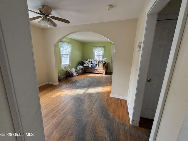 hallway featuring arched walkways, baseboards, and wood finished floors