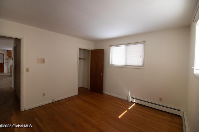 unfurnished bedroom featuring a baseboard heating unit, a closet, baseboards, and wood finished floors