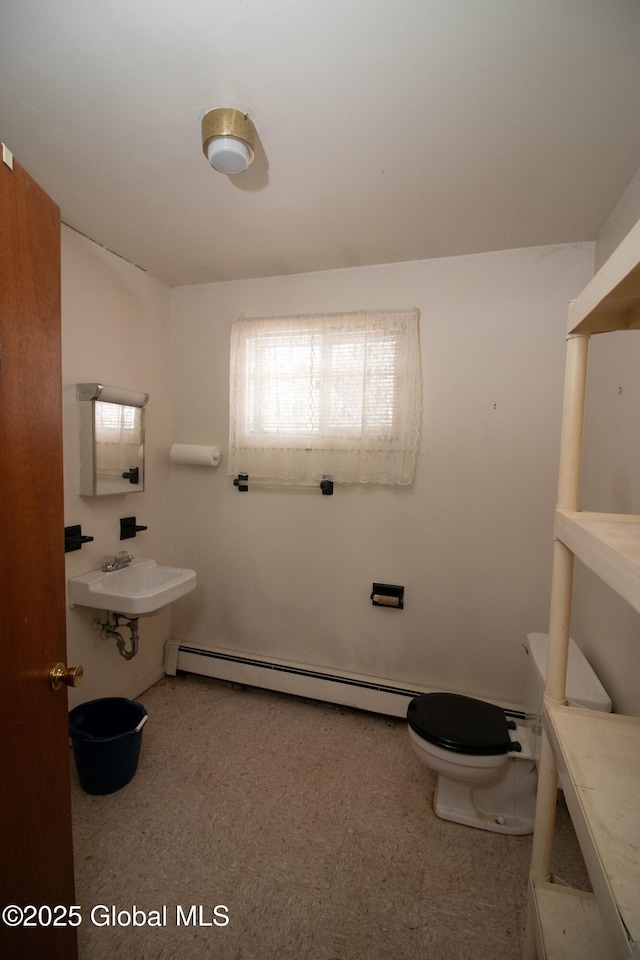 half bath with toilet, a baseboard heating unit, and a sink