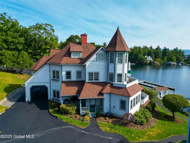 view of front facade featuring driveway, a chimney, roof with shingles, a water view, and a porch