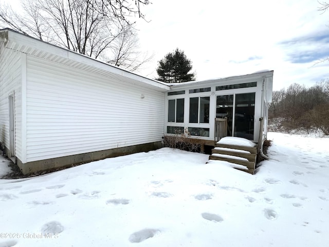 snow covered rear of property featuring a garage and a sunroom