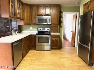 kitchen featuring a sink, light countertops, glass insert cabinets, light wood-style floors, and appliances with stainless steel finishes