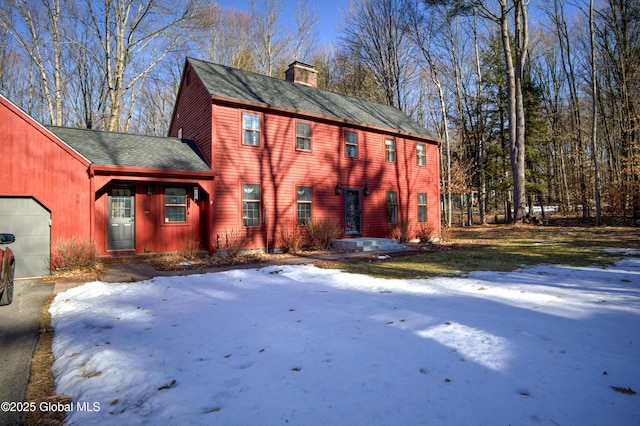 view of front of property featuring a chimney, a garage, and a shingled roof