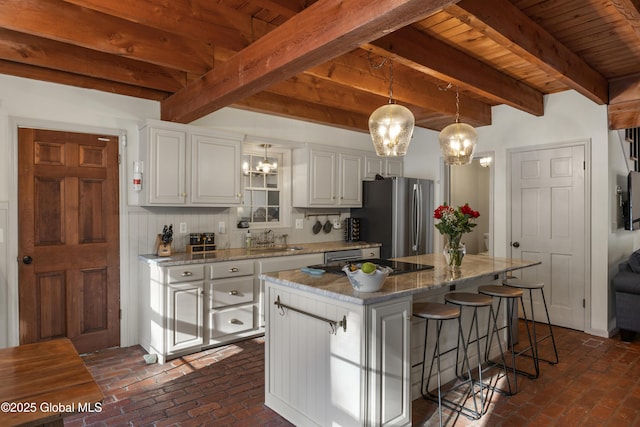 kitchen with a kitchen island, a kitchen breakfast bar, freestanding refrigerator, brick floor, and a sink