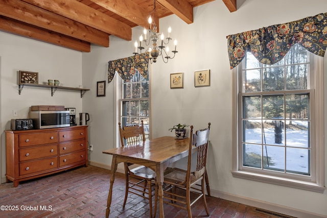 dining space featuring beam ceiling, a chandelier, baseboards, and brick floor