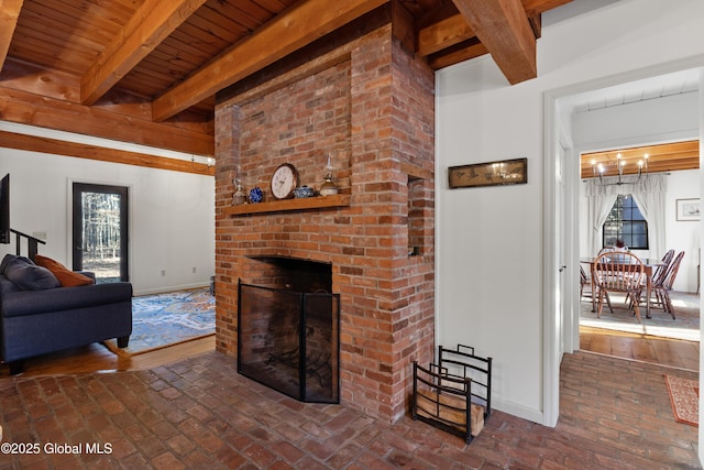 living area featuring beamed ceiling, a fireplace, brick floor, and baseboards