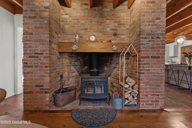 living room featuring beamed ceiling, a wood stove, and wood-type flooring