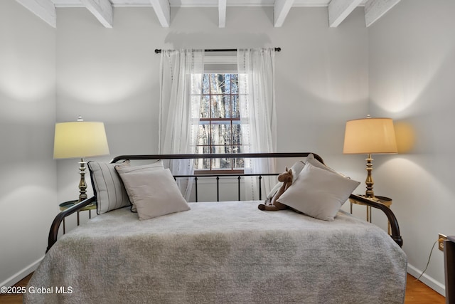 bedroom with beamed ceiling, baseboards, and wood finished floors