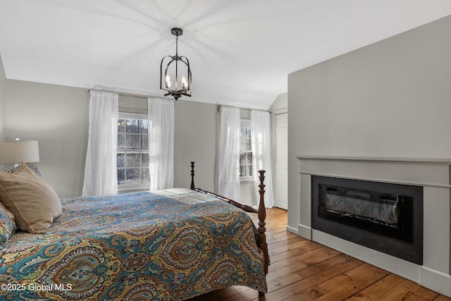 bedroom featuring baseboards, lofted ceiling, wood-type flooring, a glass covered fireplace, and a chandelier