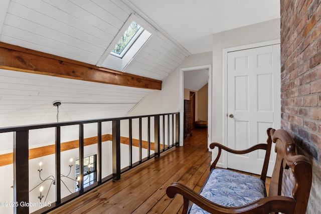 hall with vaulted ceiling with skylight, brick wall, and hardwood / wood-style flooring