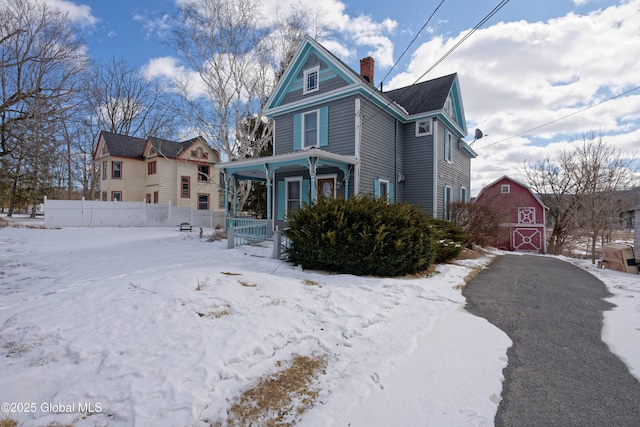 view of front facade featuring a chimney, a porch, fence, a barn, and an outdoor structure