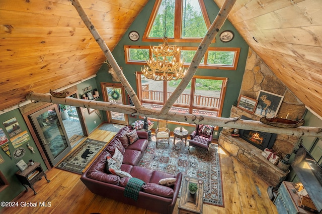 living room with wood ceiling, hardwood / wood-style floors, an inviting chandelier, vaulted ceiling, and a stone fireplace