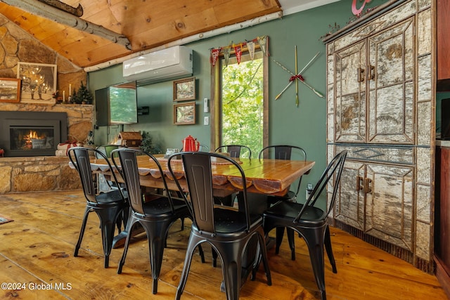 dining room featuring lofted ceiling, hardwood / wood-style flooring, an AC wall unit, and a stone fireplace