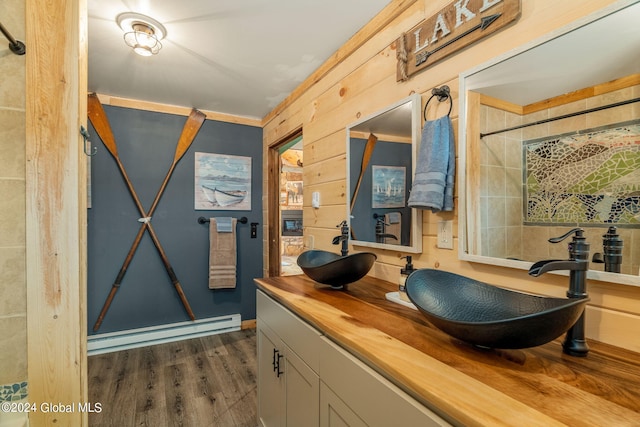 full bath featuring a sink, double vanity, baseboard heating, and wood finished floors