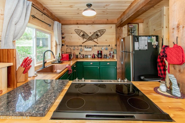 kitchen featuring butcher block counters, freestanding refrigerator, wood walls, green cabinets, and a sink