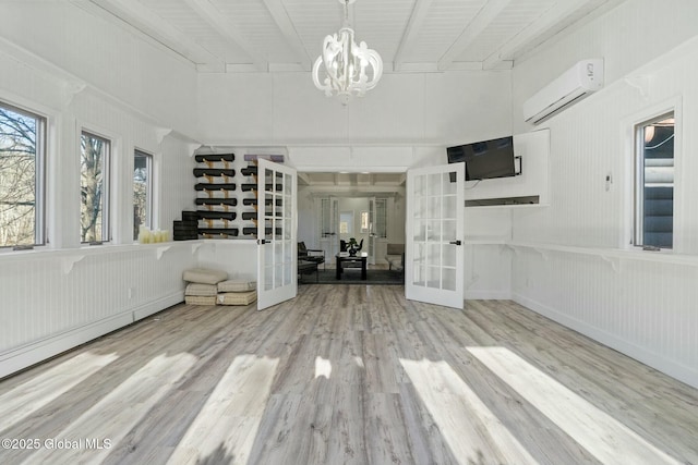 interior space with french doors, a wall mounted air conditioner, beamed ceiling, and wood finished floors