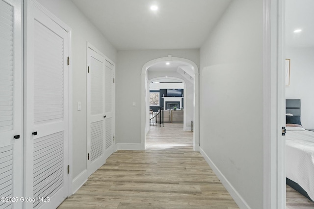 hall featuring arched walkways, recessed lighting, light wood-type flooring, and baseboards