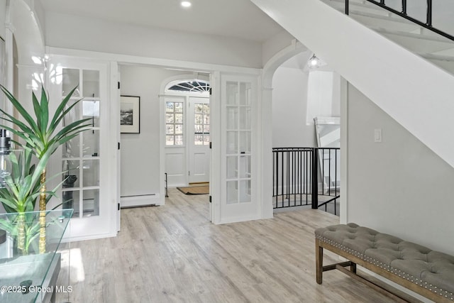 foyer entrance with arched walkways, a baseboard heating unit, french doors, and wood finished floors