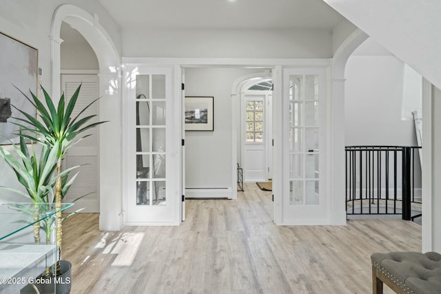 entrance foyer featuring arched walkways, baseboard heating, and wood finished floors