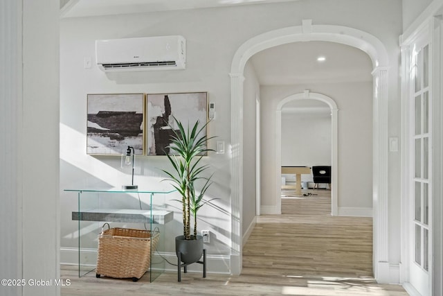 hallway featuring arched walkways, an AC wall unit, baseboards, and wood finished floors