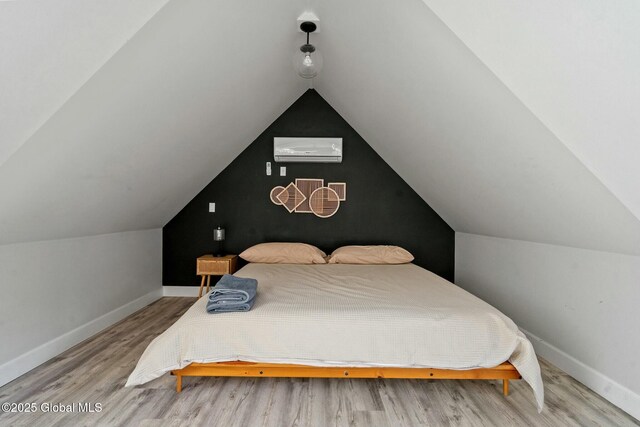 bedroom with baseboards, vaulted ceiling, wood finished floors, and a wall mounted air conditioner