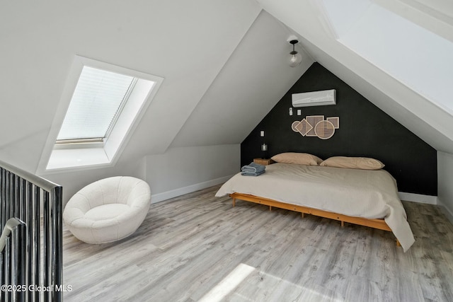 bedroom featuring vaulted ceiling with skylight, a wall unit AC, baseboards, and wood finished floors