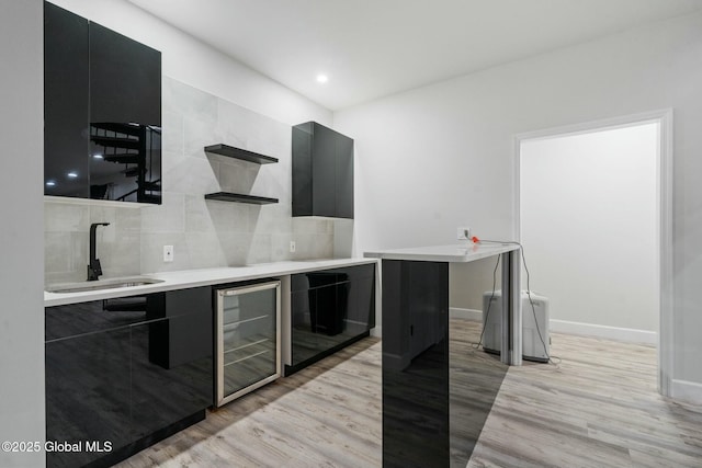 kitchen with modern cabinets, wine cooler, dark cabinetry, and a sink