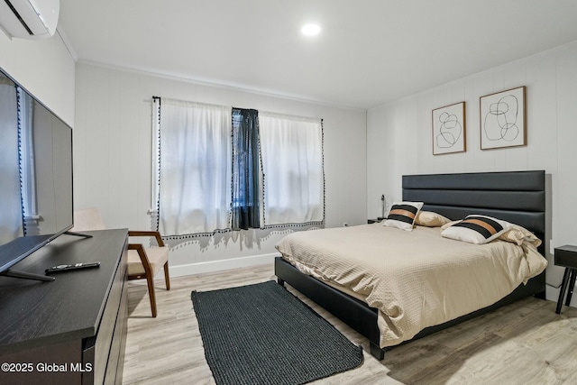 bedroom featuring light wood-style flooring, crown molding, baseboards, and an AC wall unit