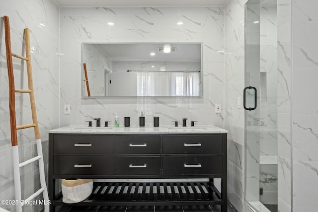 full bathroom with a sink, tile walls, a marble finish shower, and double vanity