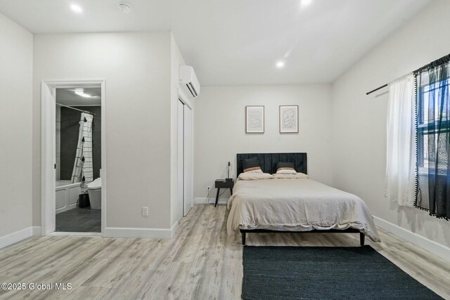 bedroom featuring recessed lighting, wood finished floors, baseboards, an AC wall unit, and ensuite bath