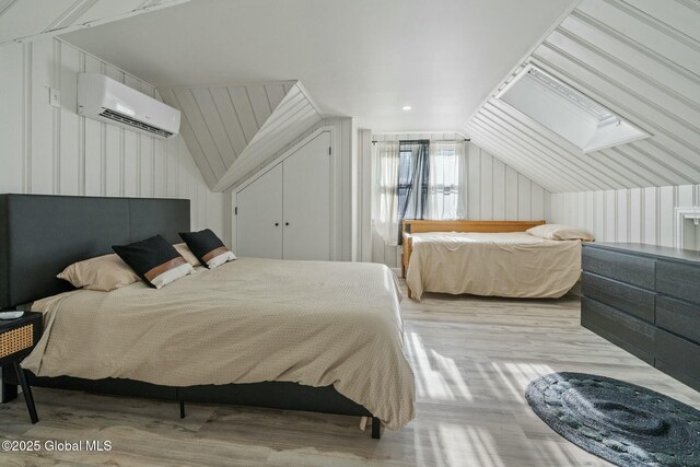 bedroom featuring vaulted ceiling with skylight, a wall unit AC, and wood finished floors