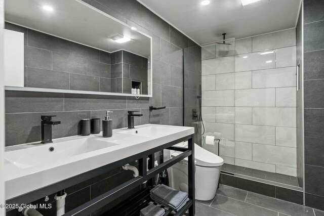 full bath featuring toilet, a sink, tile walls, tiled shower, and decorative backsplash