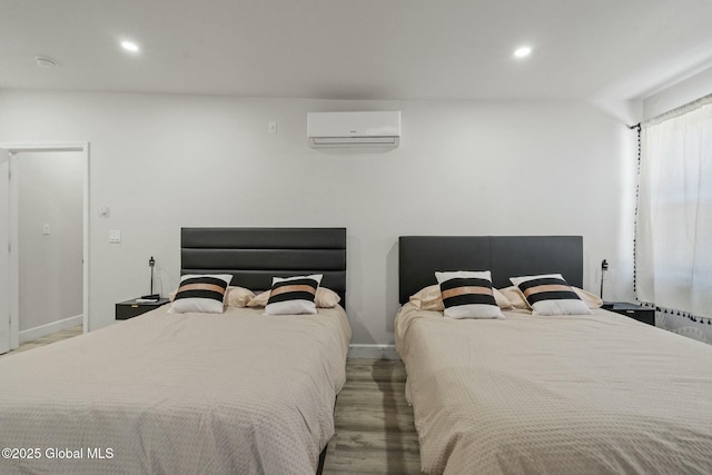 bedroom featuring a wall unit AC, baseboards, wood finished floors, and recessed lighting