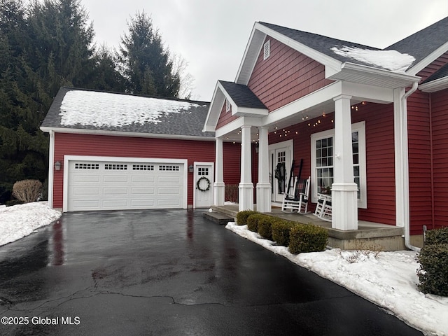 view of side of property with an attached garage, driveway, a porch, and a shingled roof