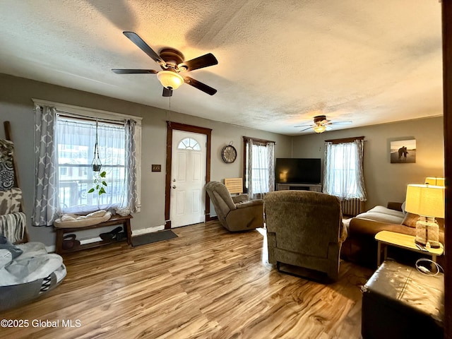 living room featuring ceiling fan, a textured ceiling, baseboards, and wood finished floors