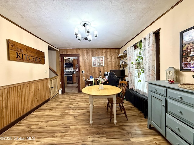 dining room featuring light wood finished floors, a chandelier, a textured ceiling, and ornamental molding