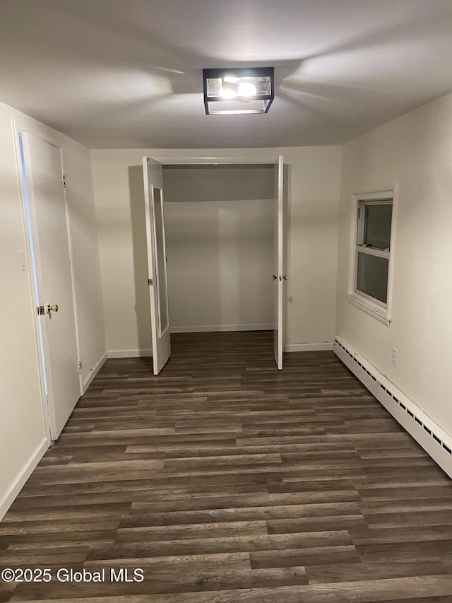 spare room with baseboards, baseboard heating, and dark wood-type flooring