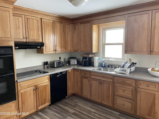 kitchen featuring dark wood finished floors, brown cabinetry, under cabinet range hood, black appliances, and a sink