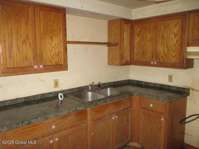 kitchen featuring dark countertops, under cabinet range hood, brown cabinets, and a sink