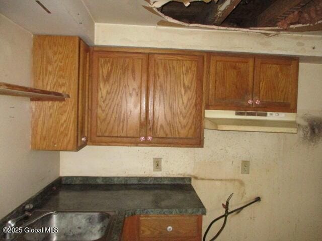 kitchen featuring dark countertops, brown cabinets, a sink, and under cabinet range hood