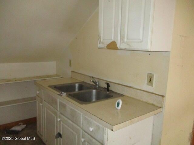 kitchen with vaulted ceiling, light countertops, a sink, and white cabinets