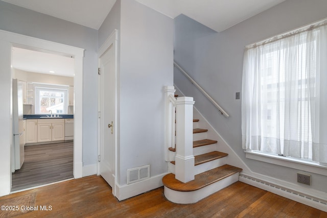 staircase featuring a baseboard heating unit, visible vents, and wood finished floors