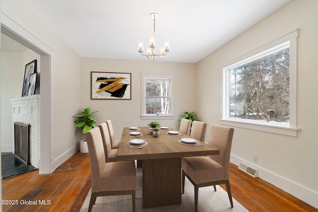 dining space with a fireplace, wood finished floors, visible vents, baseboards, and an inviting chandelier