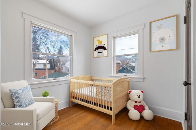 bedroom featuring a crib, baseboards, and wood finished floors