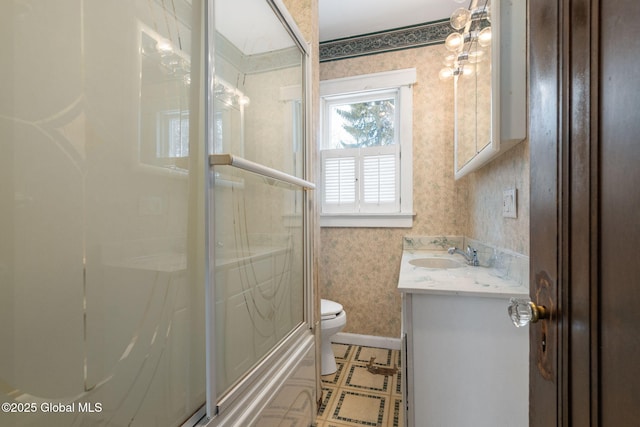 bathroom featuring toilet, vanity, baseboards, a shower with door, and wallpapered walls