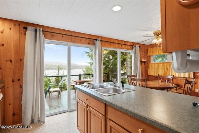 536 E Shore Dr, Horicon, NY 12808 - kitchen featuring a sink, wood walls, a ceiling fan, a water view, and brown cabinetry