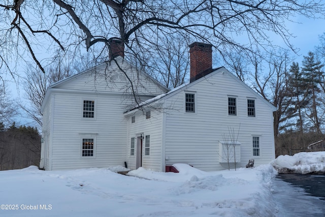 snow covered back of property featuring a garage and a chimney